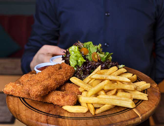 A waite holding a plate of organic fish and chips, served from our Cafe Newton.