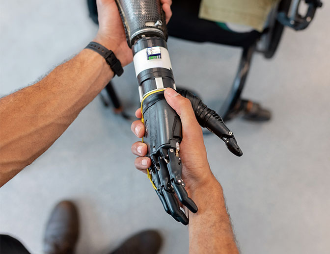 A volunteer at CSM is helping a man with a robotic hand.